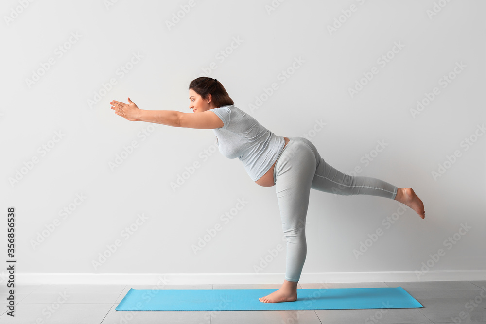 Young pregnant woman practicing yoga near light wall