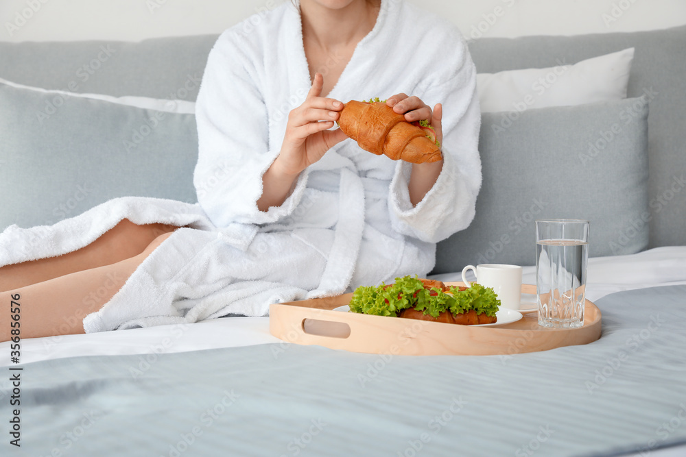 Young woman having breakfast on bed in hotel room