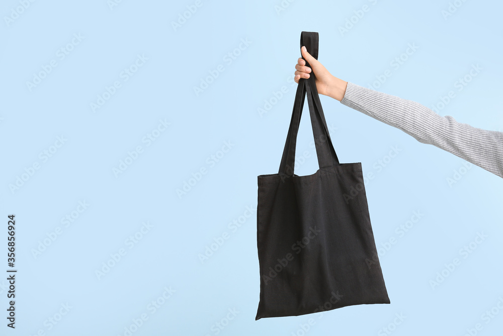 Female hand with eco bag on color background