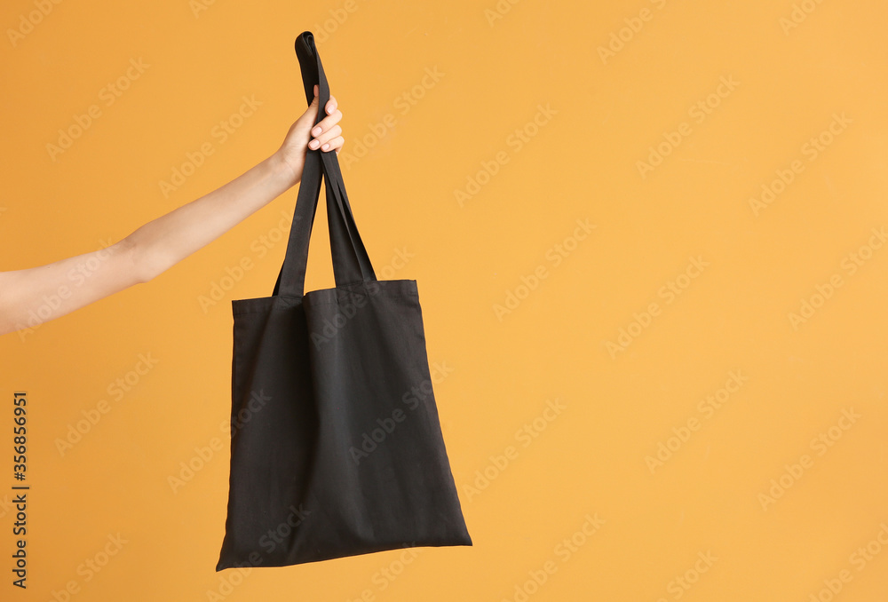 Female hand with eco bag on color background