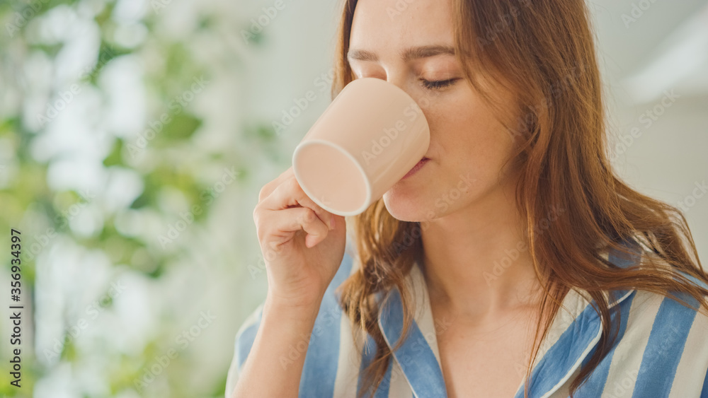 一位美丽的年轻女性在家里明亮的房间里喝茶或喝咖啡的真实肖像