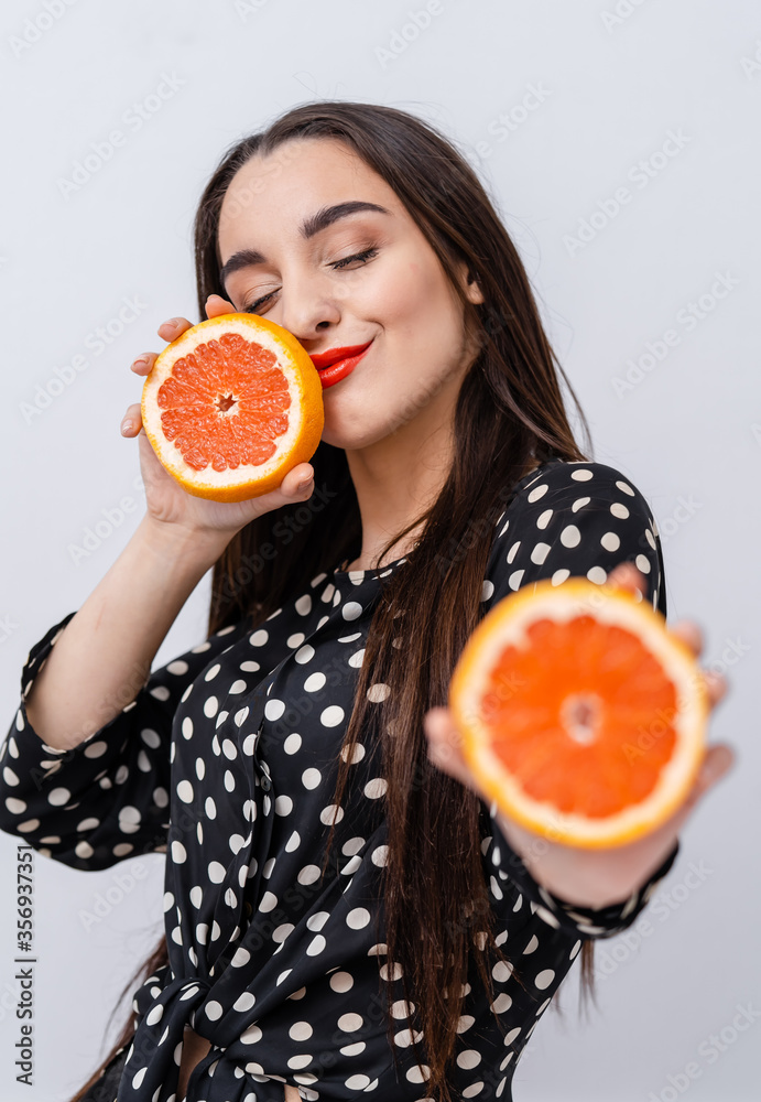 Cute woman with red lips. Woman holding citrus fruit halves in hands showing to the camera. Facial e