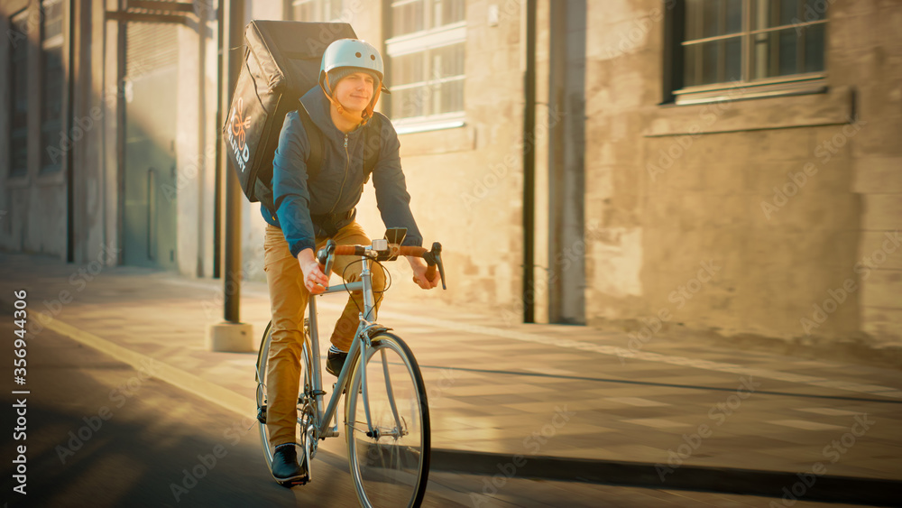 Happy Food Delivery Courier Wearing Thermal Backpack Rides a Bike on the Road To Deliver Orders for 