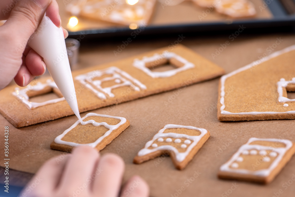 Young woman is decorating Christmas Gingerbread House cookies biscuit at home with frosting topping 