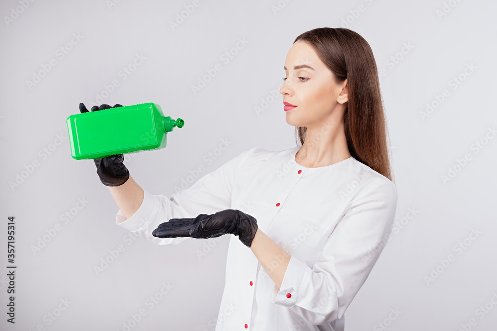 girl in black gloves pours liquid from green can, disinfectant solution, light gray background, woma