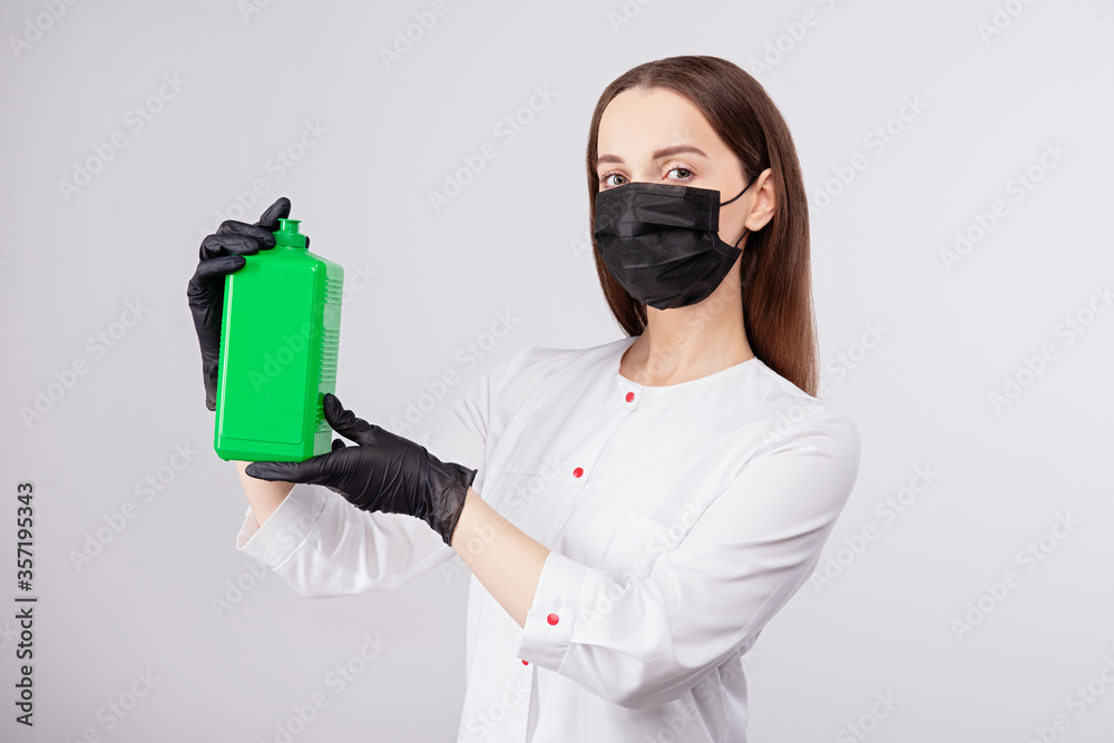 disinfectant in green jar, girl in mask and gloves holds an antiseptic in her hands, light gray back