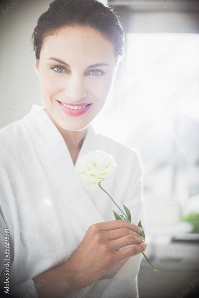 Portrait of smiling woman in bathrobe holding white rose