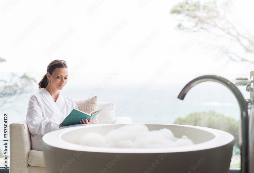 Smiling woman in bathrobe reading book in bathroom