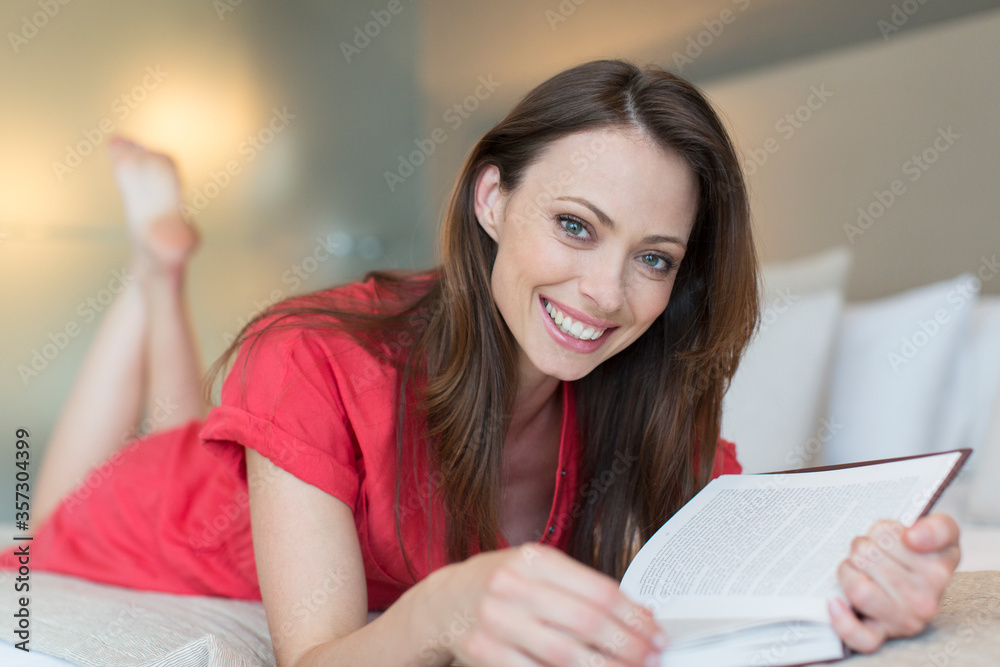 Portrait of smiling woman lying on bed and reading book