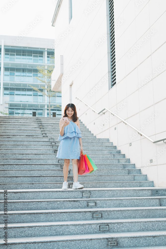 亚洲年轻女子下楼梯，手里拿着购物袋，购物狂概念