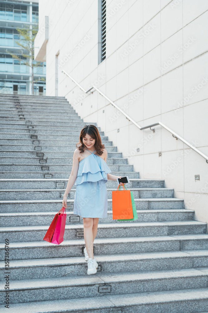 Portrait of young Asian woman going down stairs with color shopping bag. Lifestyle and shopping conc