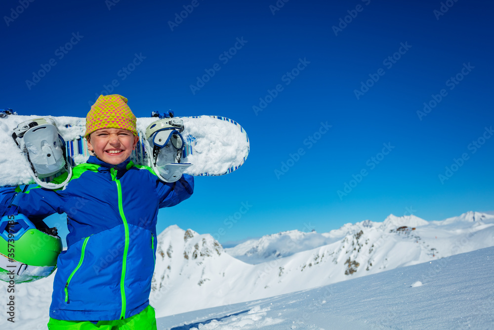 一个男孩肩上扛着滑雪板和休闲帽俯瞰山脉全景的近景