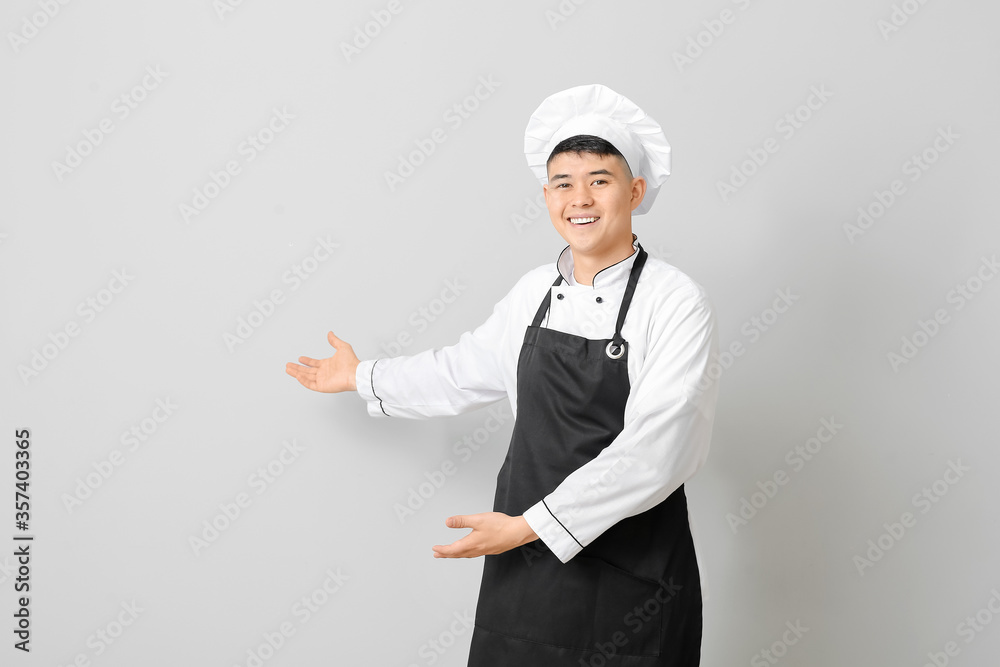 Handsome Asian chef showing something on grey background