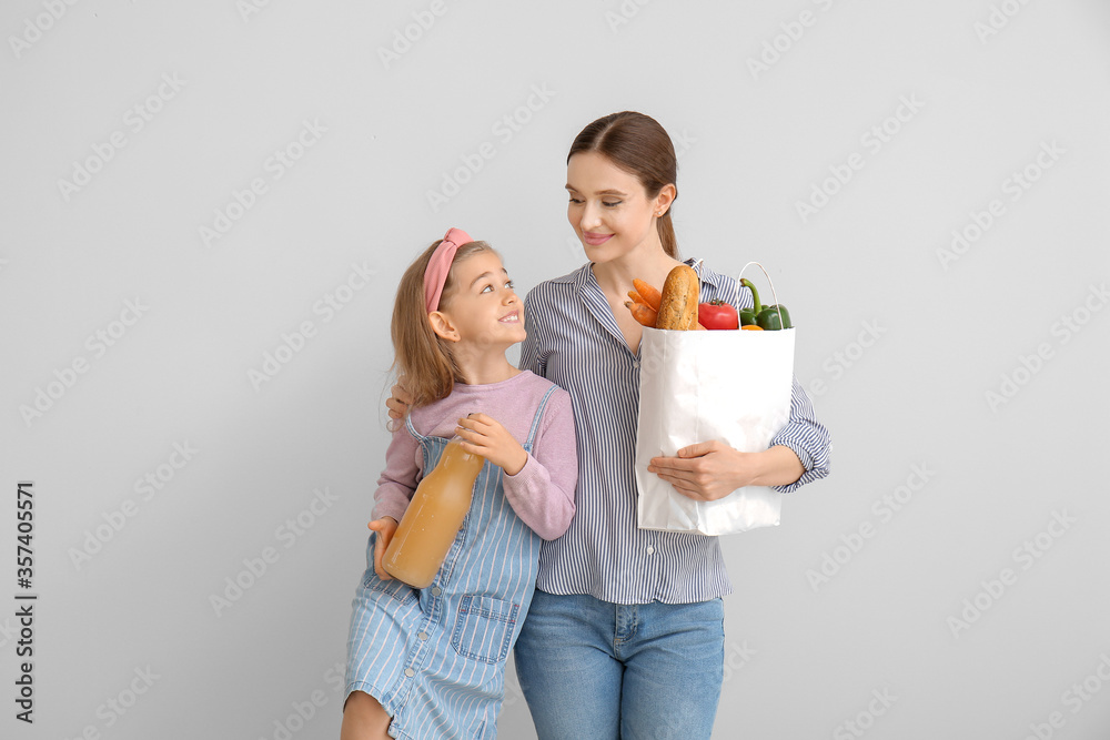 Mother and daughter with food in bag on light background