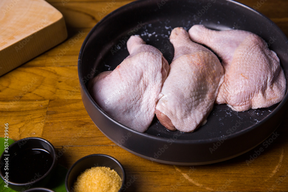 Raw chicken legs on a black plate, meat with ingredients for cooking