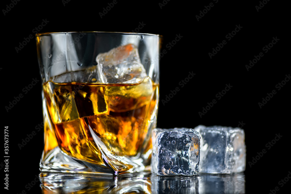 Glass of whiskey with cube ice on black background