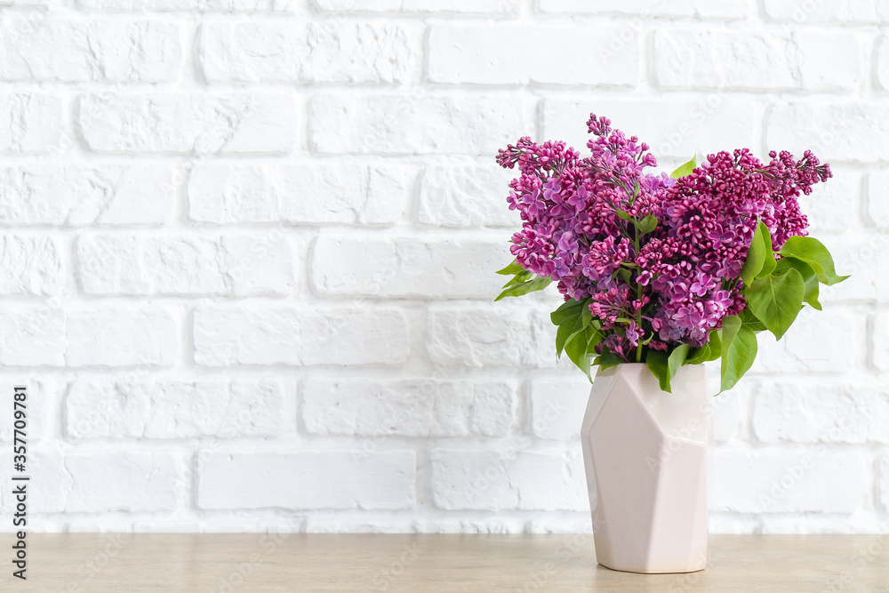 Vase with beautiful flowers on table near white brick wall