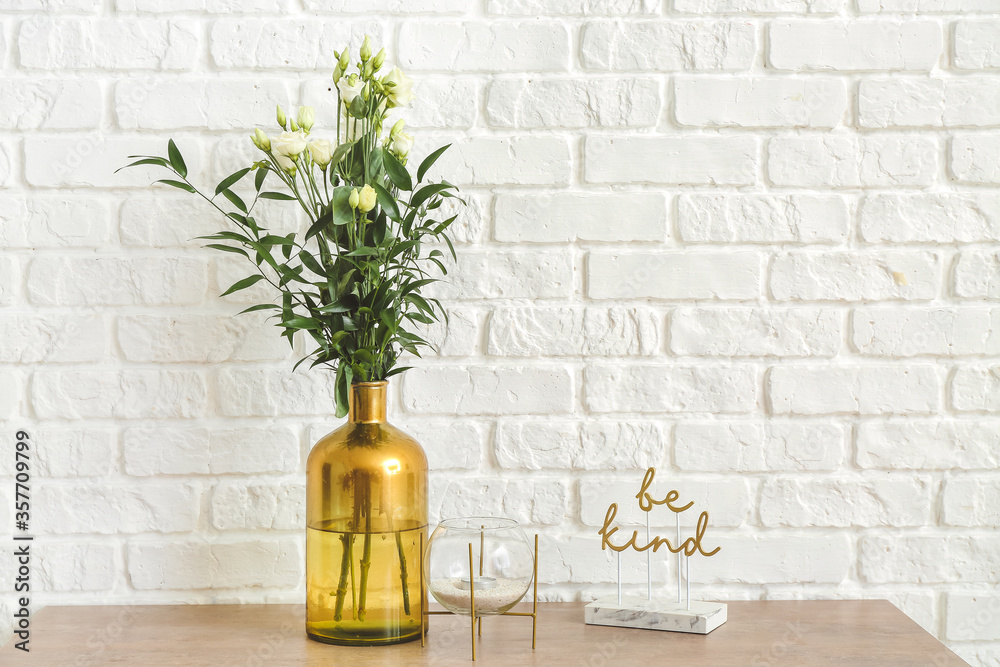 Vase with beautiful flowers and candle near white brick wall