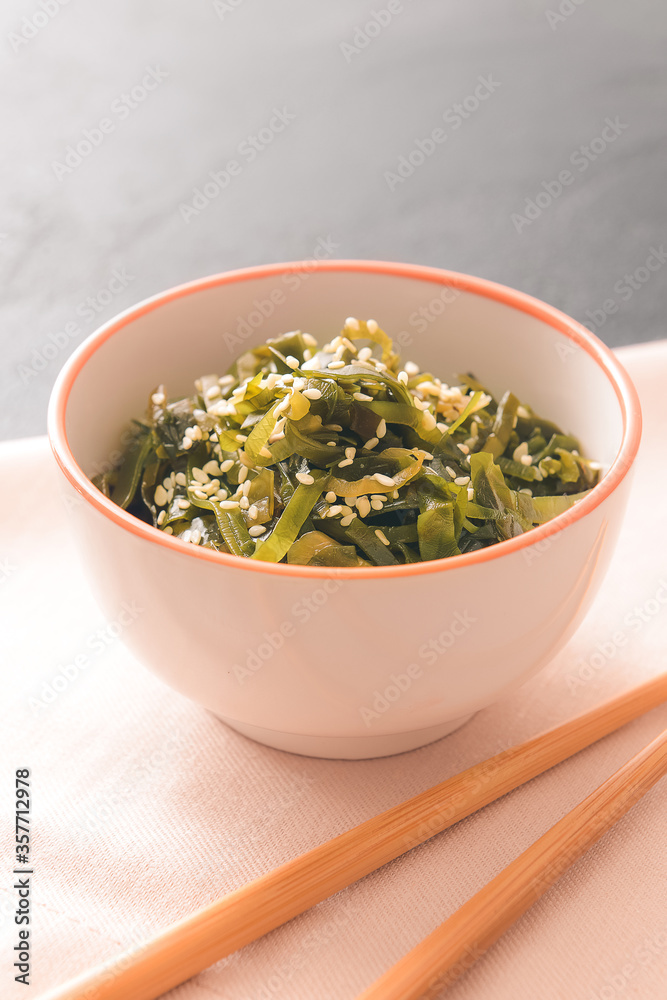 Bowl with tasty seaweed and chopsticks on table