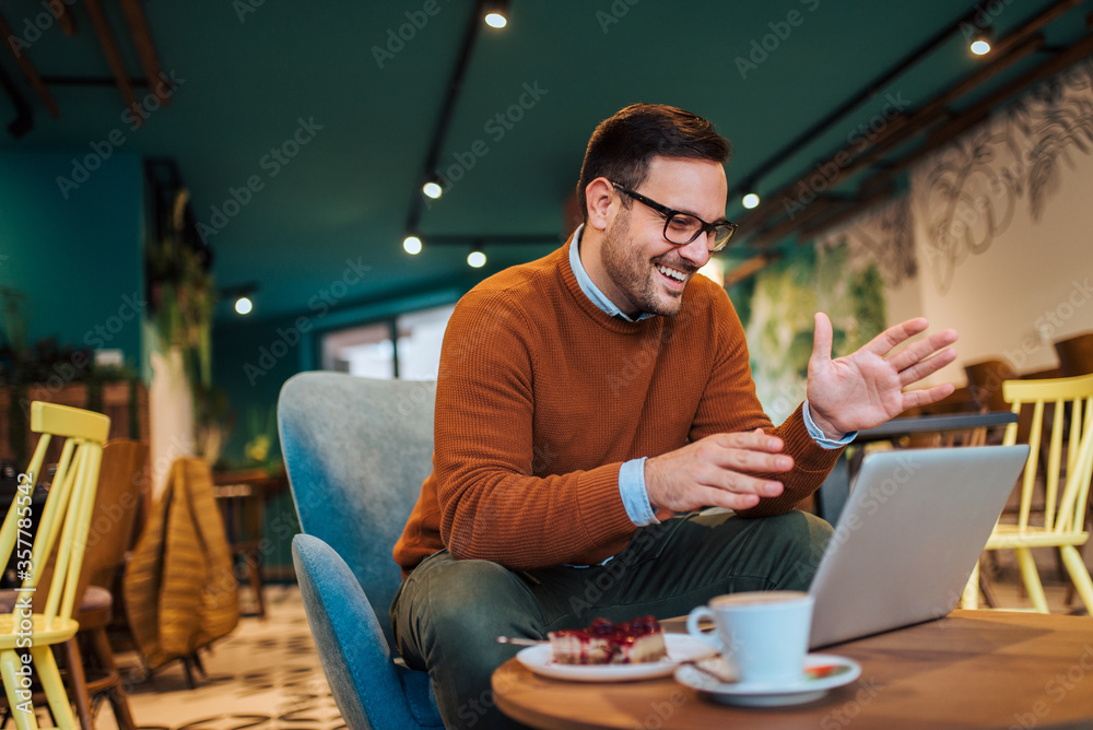 Handsome smiling man having video call on laptop in the cafe.