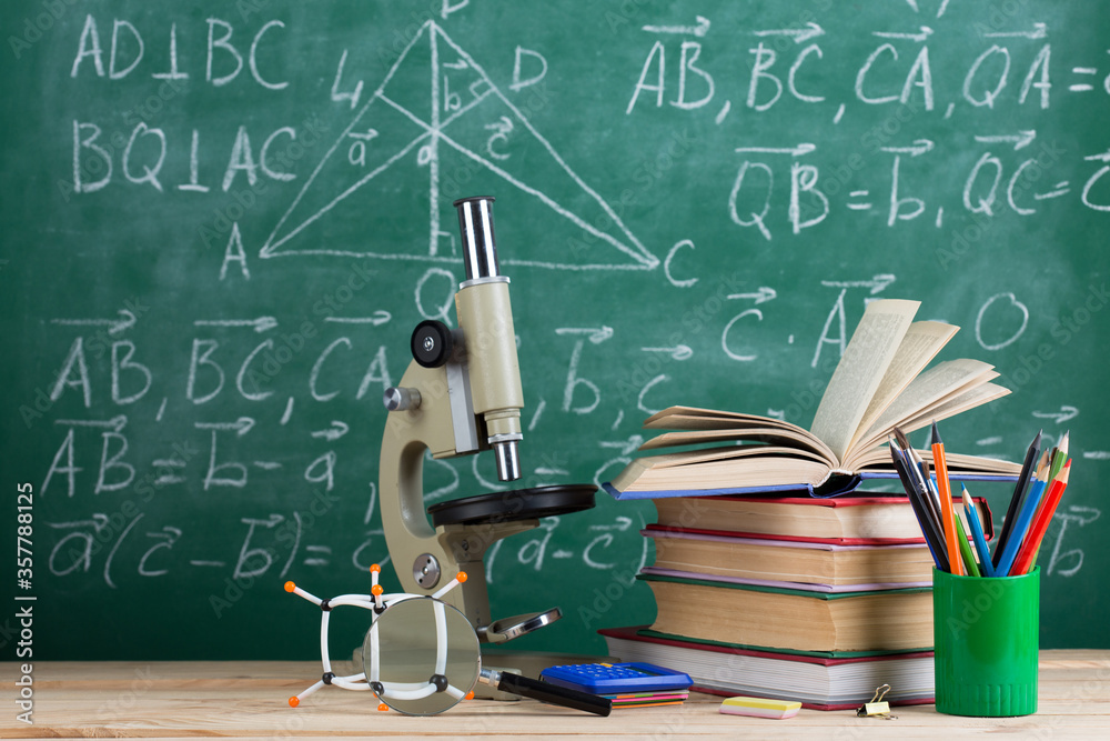 Education and sciences concept - books, molecule model and microscope on the desk in the auditorium,