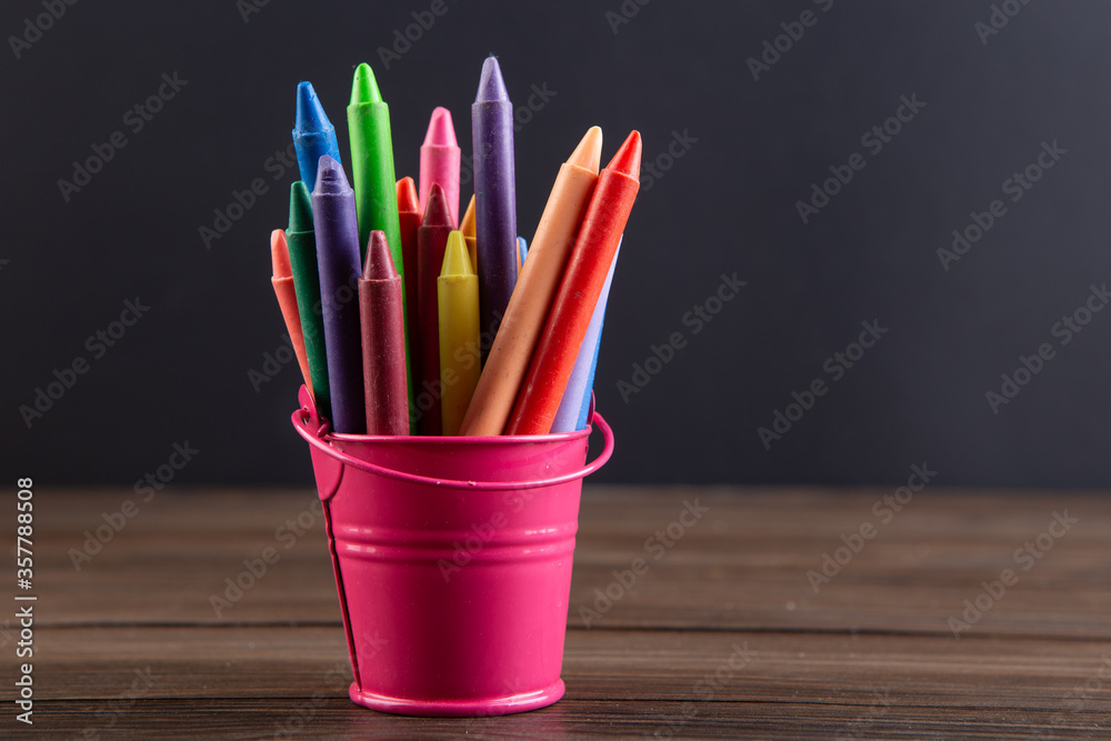 colored crayons on the wooden table, blackboard background