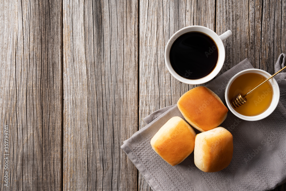 Dinner rolls, coffee and honey set against an old wooden backdrop