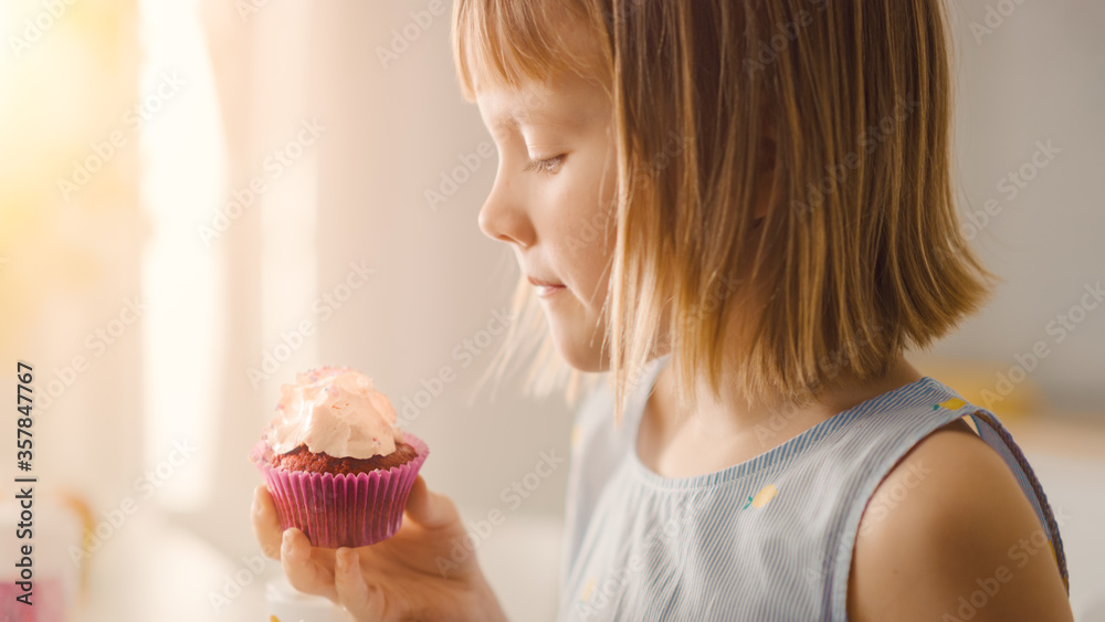 In the Kitchen: Adorable Little Girl Eats Creamy Cupcake with Frosting and Sprinkled Confetti. Cute 