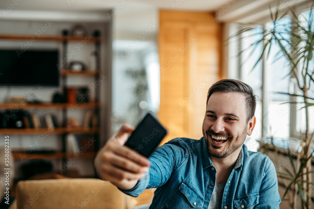 Cheerful man taking selfie on smart phone at home, portrait.