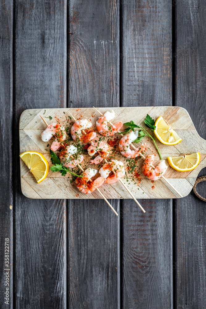 Shrimp skewers - seafood snack - on cutting bioard on wooden table top view copy space