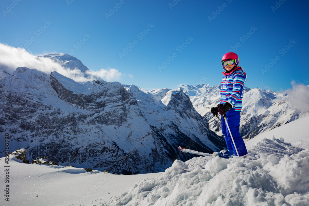 Portrait of a ski girl stand on snow pile in colorful vivid sport clothes, helmet and glasses over A