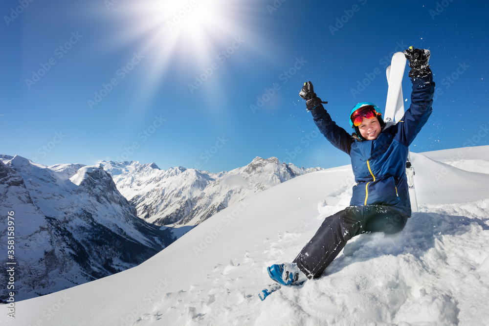 山上的肖像，一个戴着蓝色头盔、穿着滑雪服的女孩坐在雪地上