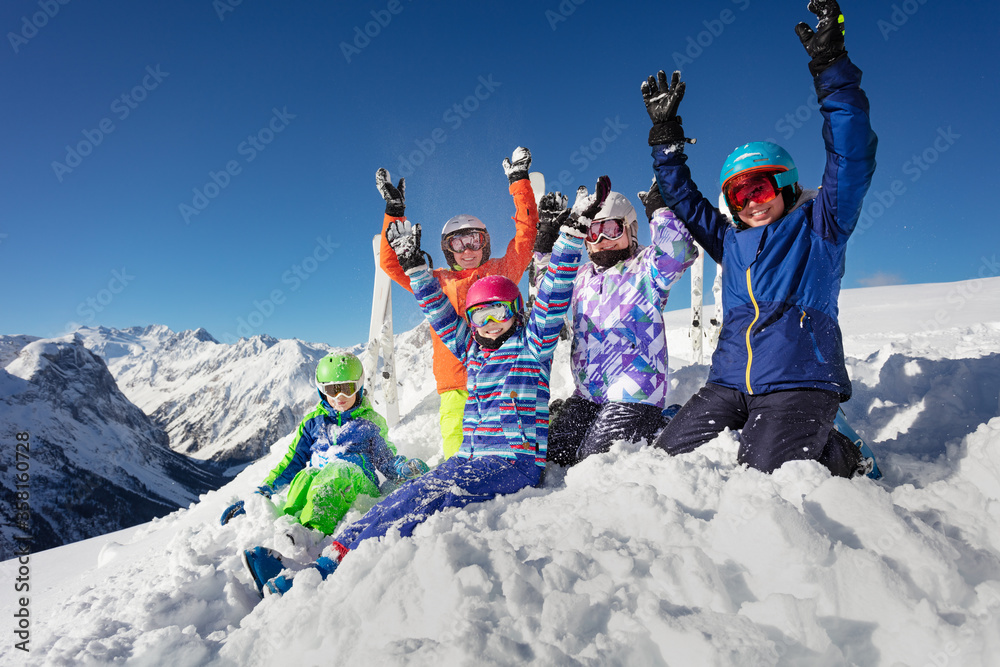 一大群滑雪孩子穿着五颜六色的运动服坐在山脉山峰上的积雪上