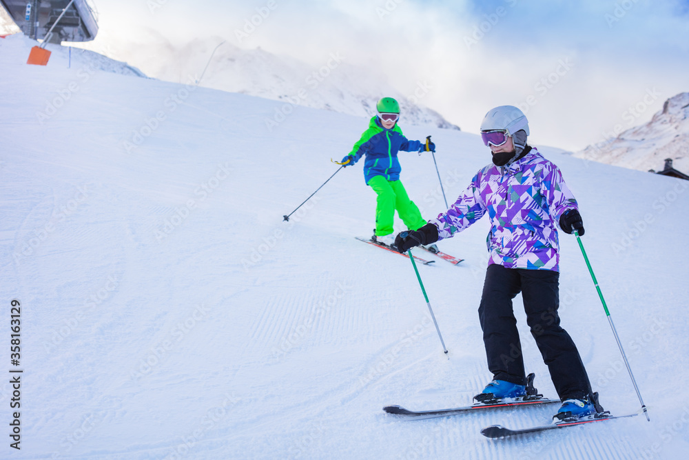 两个孩子穿着五颜六色的衣服在阿尔卑斯山的山坡上一起滑雪