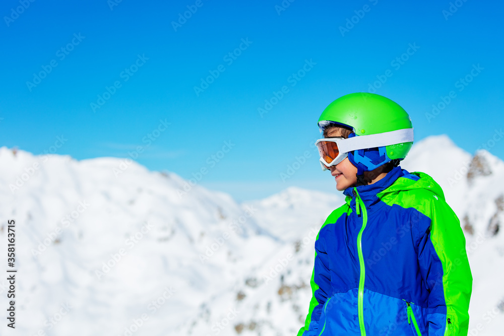 一个戴着运动头盔、戴着滑雪或滑雪板眼镜的男孩在阳光明媚的山上的近景