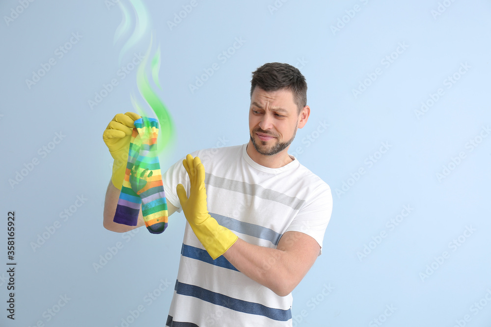 Displeased man with dirty stinky socks on light background