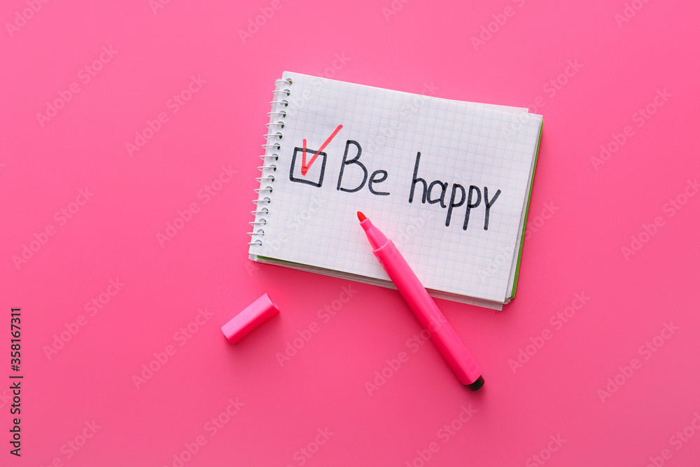 Notebook with text BE HAPPY and marker on color background