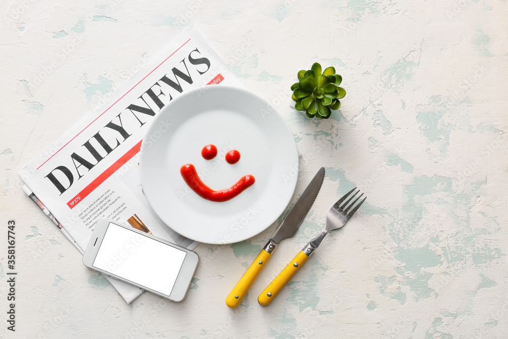 Happy face made of sauce on plate, cutlery, mobile phone and newspaper on white background