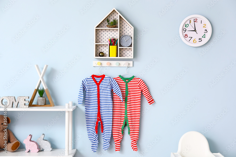 Shelf and baby clothes hanging on color wall