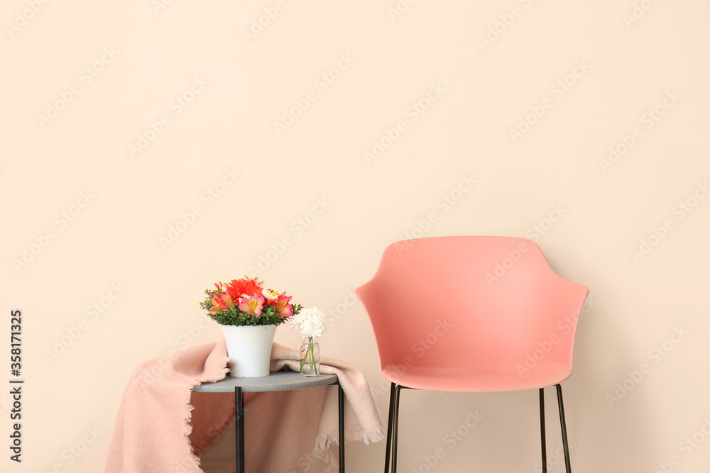 Armchair and table with flowers and plaid near color wall in living room