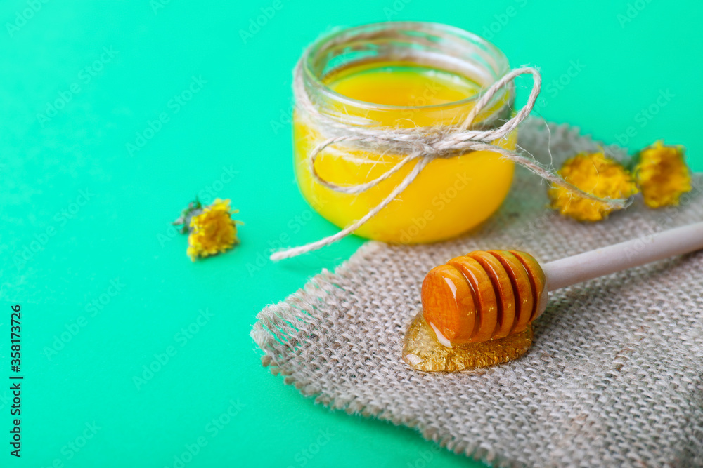 Jar of dandelion honey on color background