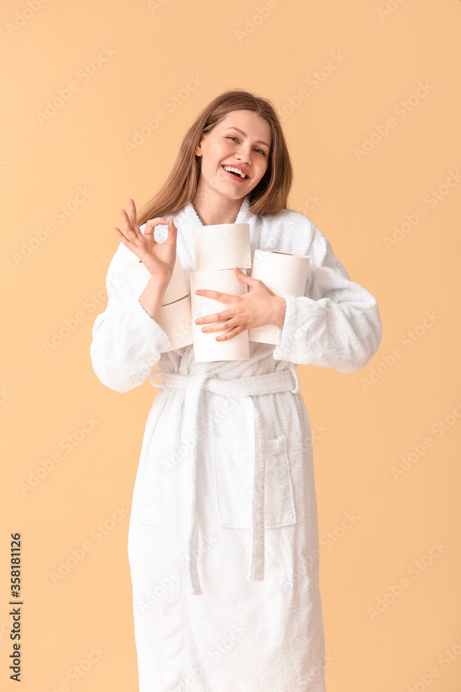 Young woman with many rolls of toilet paper showing OK on color background