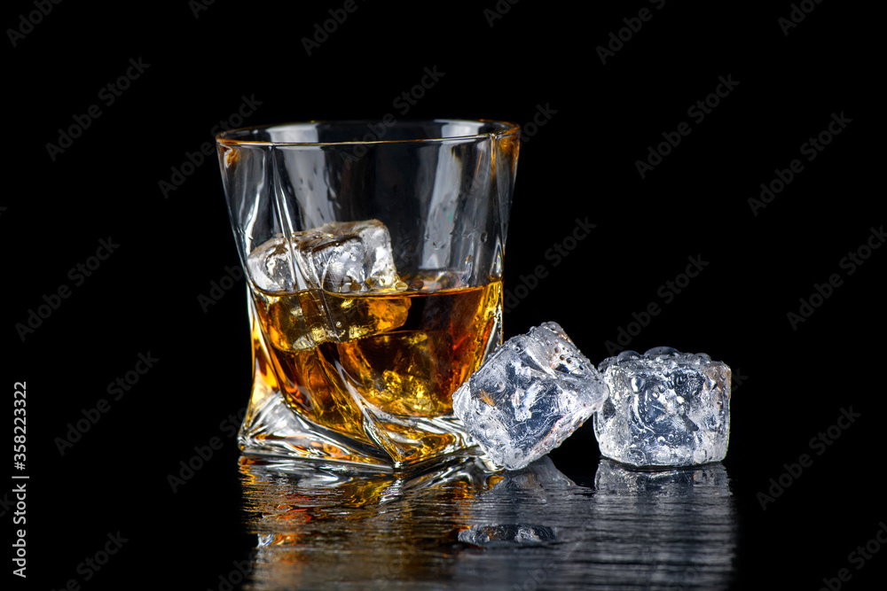 Glass of whiskey with cube ice on black background