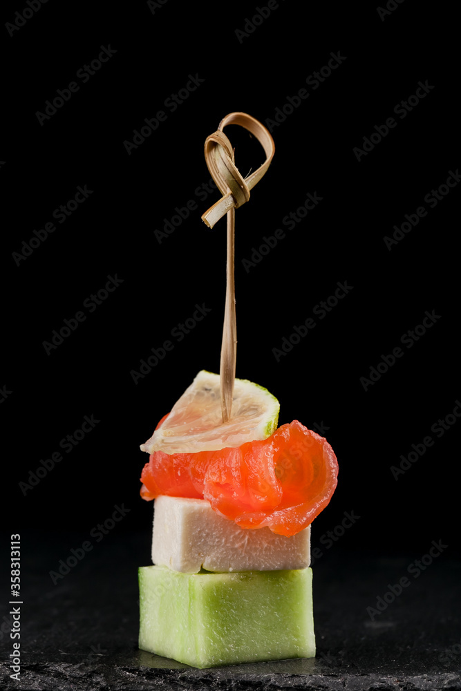 Canapé with salmon, cucumber and cheese. On a black background. Close-up.