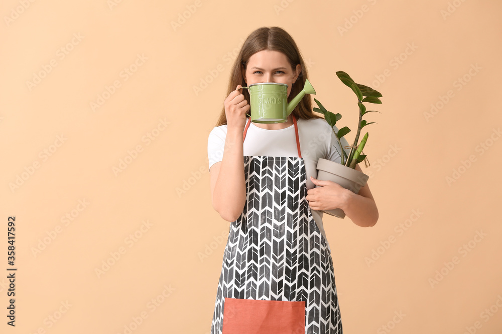 Young woman with watering can and houseplant on color background