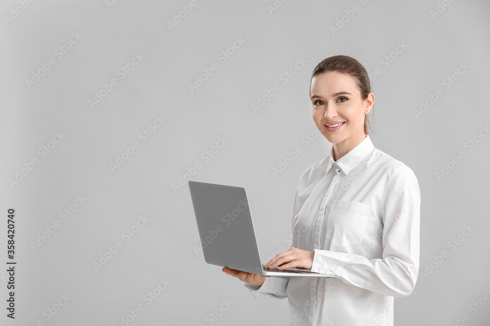 Young businesswoman with laptop on grey background