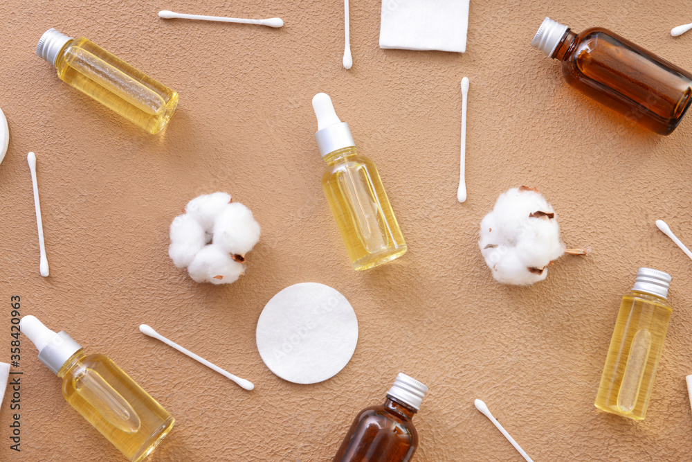 Bottles of cottonseed oil with cosmetic pads and swabs on color background