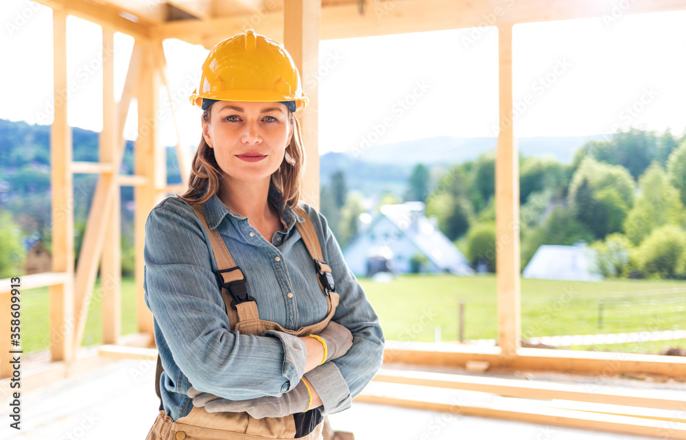 骄傲的女工人在建筑工地上摆姿势，背景是框架房屋施工