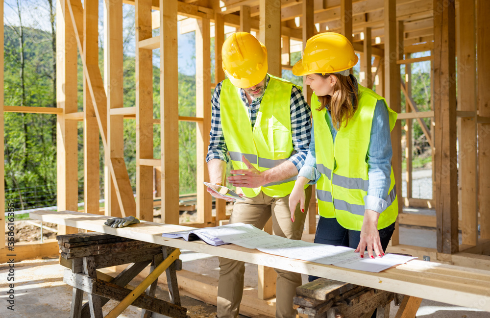 Engineers working on construction site holding blueprints of wood frame house