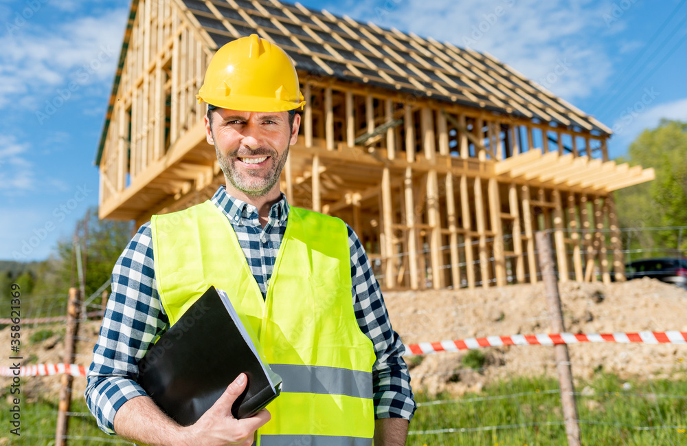 Construction engineer or architect with blueprints visiting building site of wood frame house